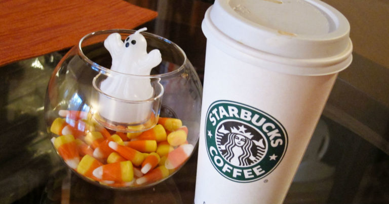 Starbucks Pumpkin Spice Latte next to a bowl of candy corn with a ghost in it