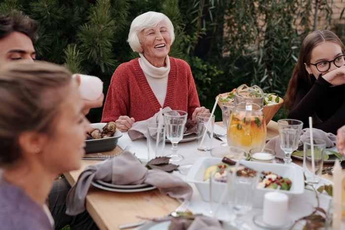 Smiling elderly woman with family and friends enjoying dinner at table backyard garden
