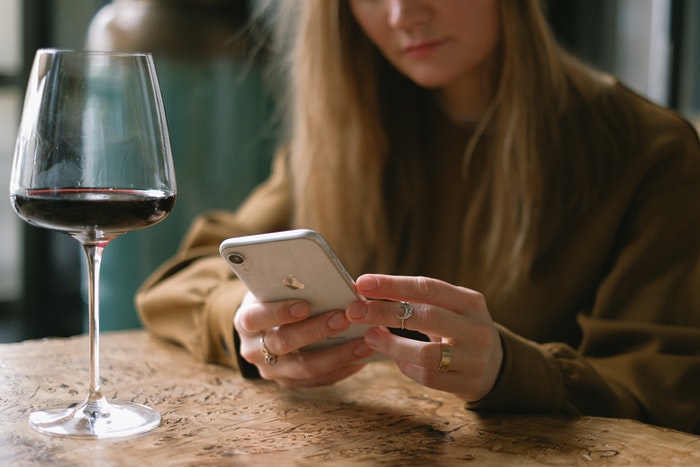 Woman Sitting with a Glass of Wine Scrolling Through Her Phone