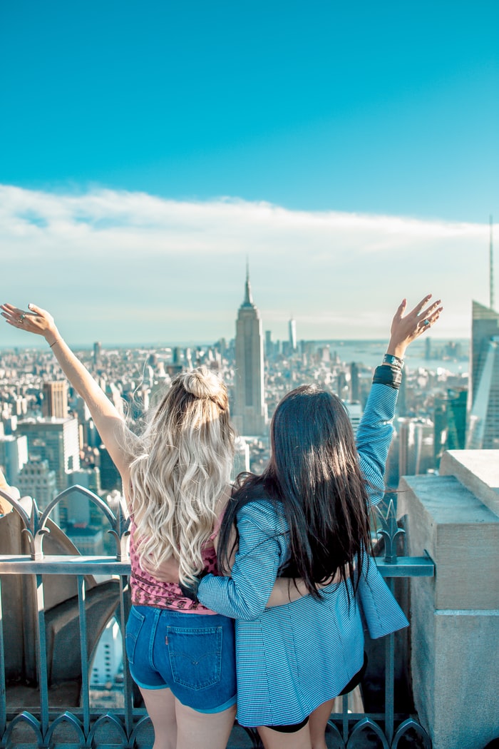 two women hands on their back while raising their hands facing Empire State building