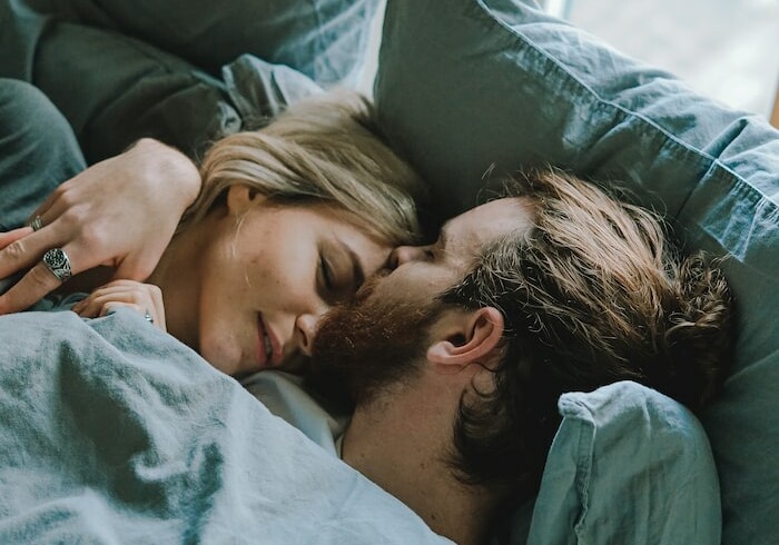 man kissing woman's forehead while lying on bed