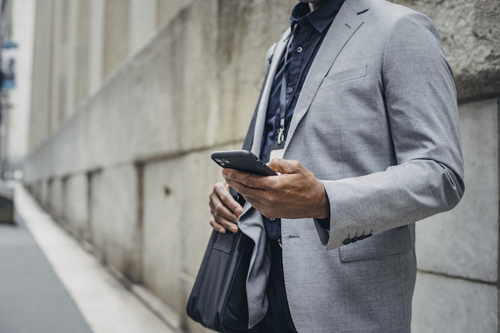Crop unrecognizable African American male in formal suit standing on street and browsing modern mobile phone