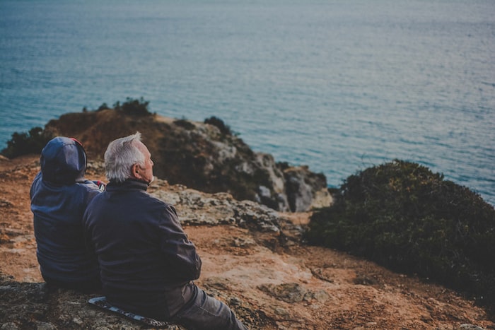 two person sitting on rock staring at body of water during daytime