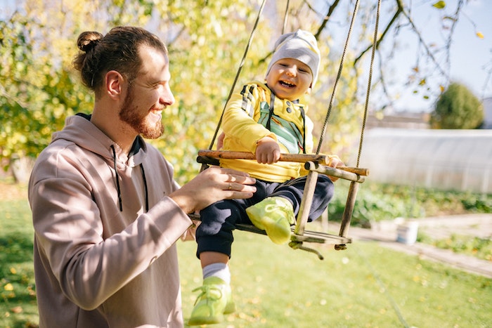 Man in Gray Coat Holding Boy in Green Shirt Riding Swing