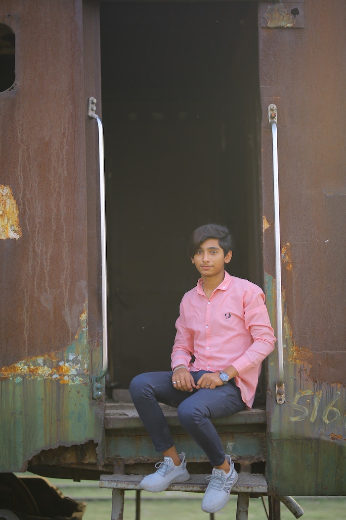 Man in Pink Dress Shirt and Blue Denim Jeans Sitting on Black Wooden Door