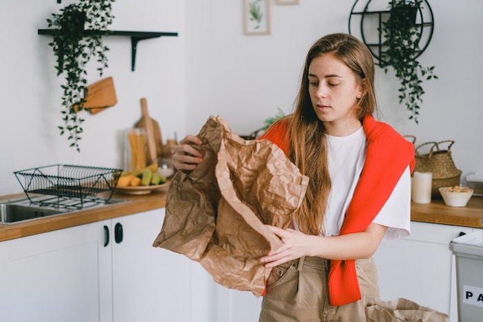 Young serious female with long hair sorting reusable paper trash in modern kitchen in apartment