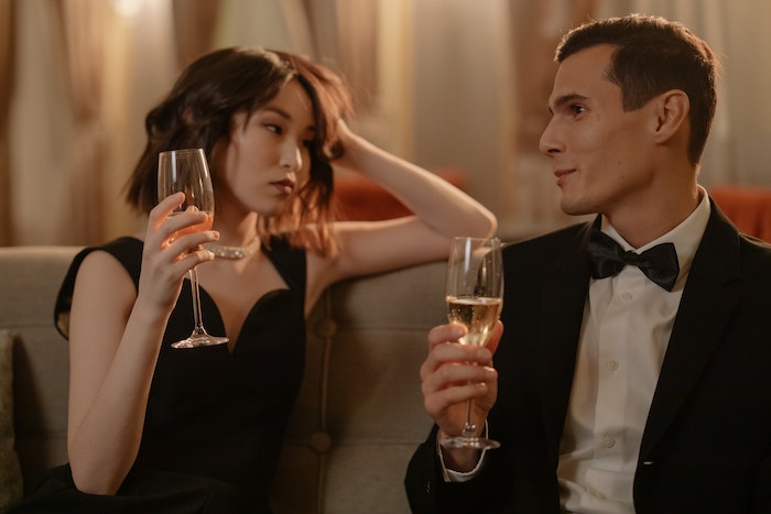 Man in Black Suit Holding Clear Drinking Glass Beside Woman in Black Sleeveless Dress